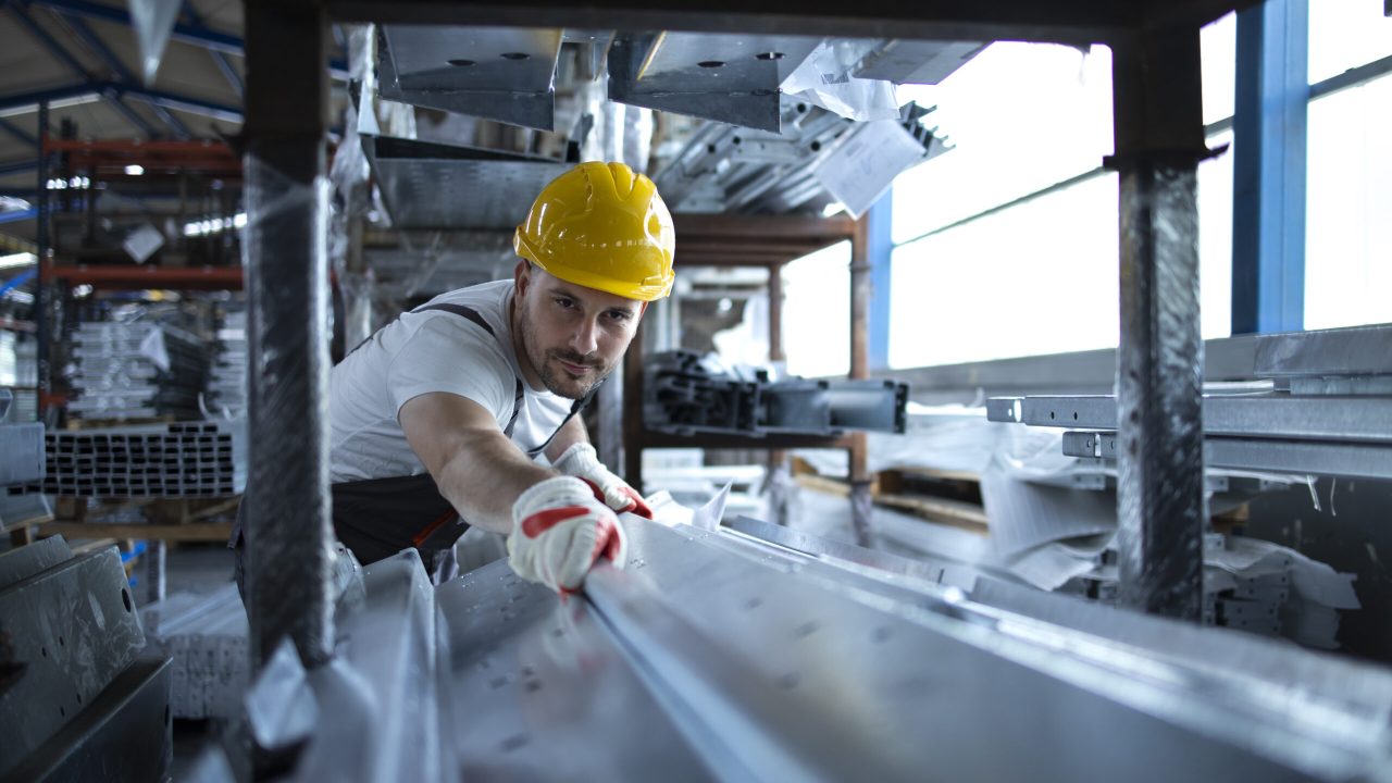 Factory worker working in warehouse handling metal material for production.